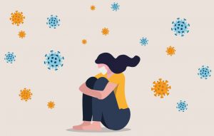 An illustration of a woman wearing a surgical mask sitting as she hugs her knees to her chest and looks down. illustrations of the covid-19 virus circle around her.